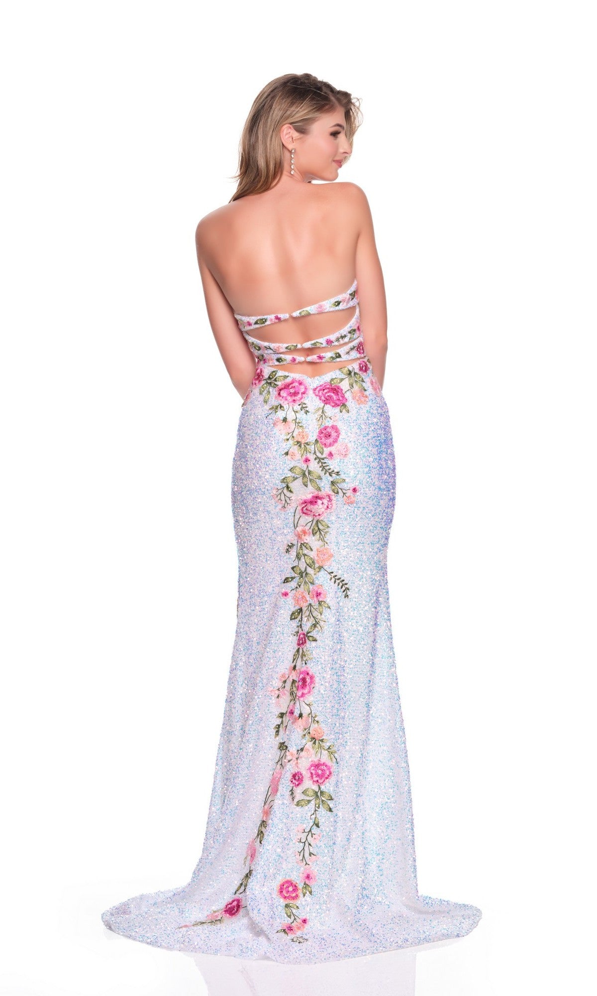 A woman poses against a plain white backdrop wearing the Dave and Johnny 12763: a backless, floor-length white prom dress with glittery floral embroidery down the back and a graceful sweetheart neckline.